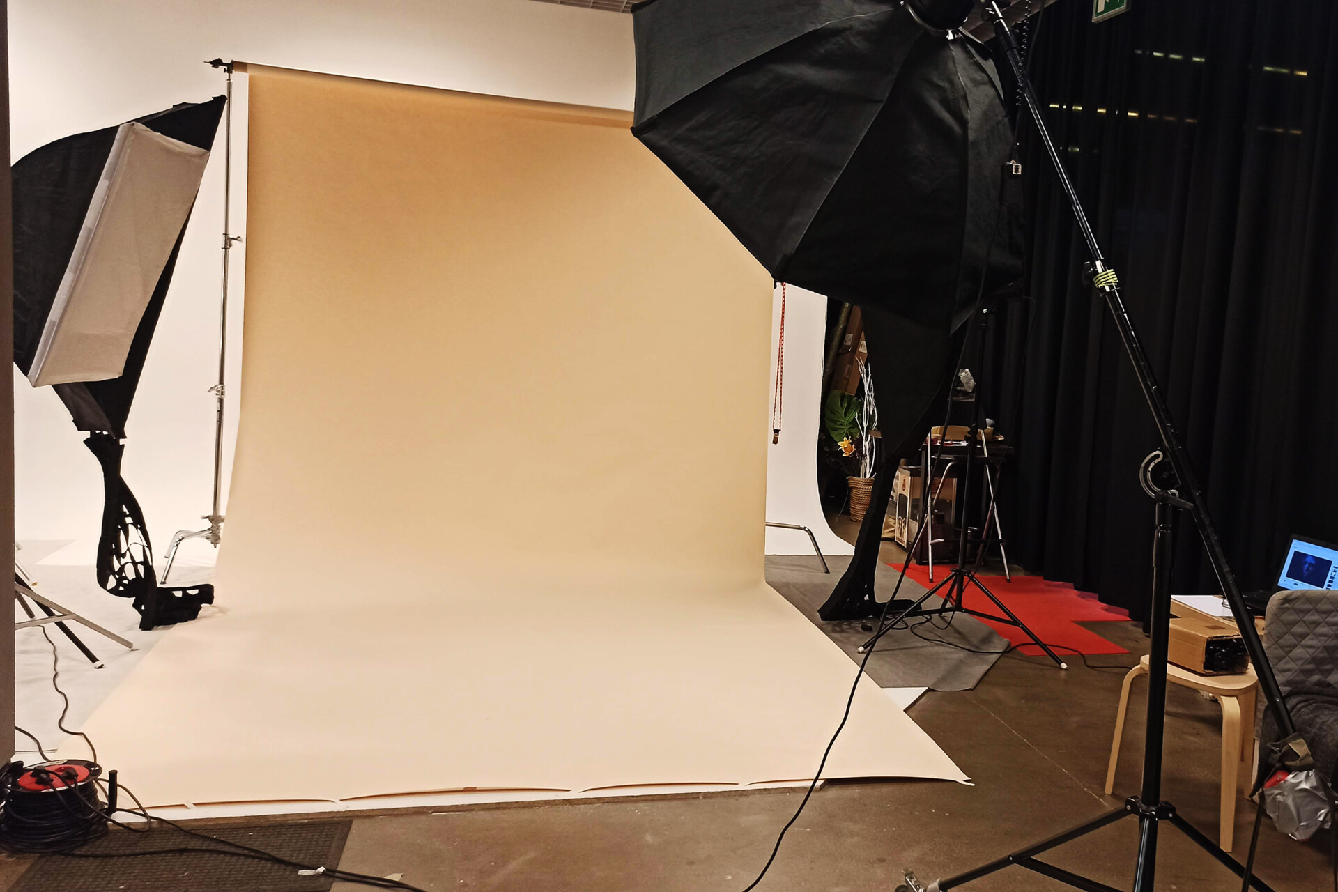 Studioska fotograficzna z beżowym tłem, dużymi lampami oraz statywami. W tle widoczna czerwona ścieżka na podłodze